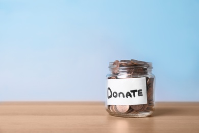Photo of Glass jar with money and label DONATE on table against color background. Space for text