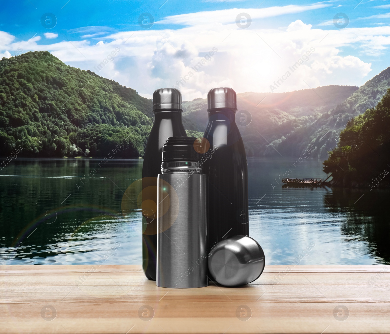 Image of Wooden desk with thermo bottles and mountain landscape on background