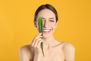 Photo of Happy young woman with aloe leaf on yellow background