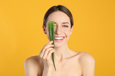 Happy young woman with aloe leaf on yellow background