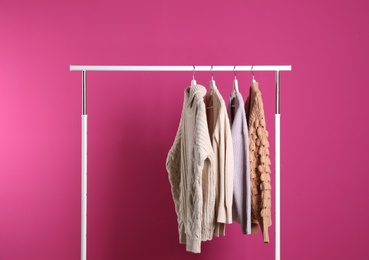 Collection of warm sweaters hanging on rack against color background