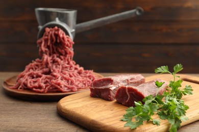 Photo of Manual meat grinder with beef and parsley on wooden table