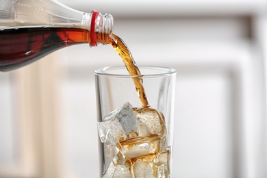 Photo of Pouring cola from bottle into glass on blurred background, closeup