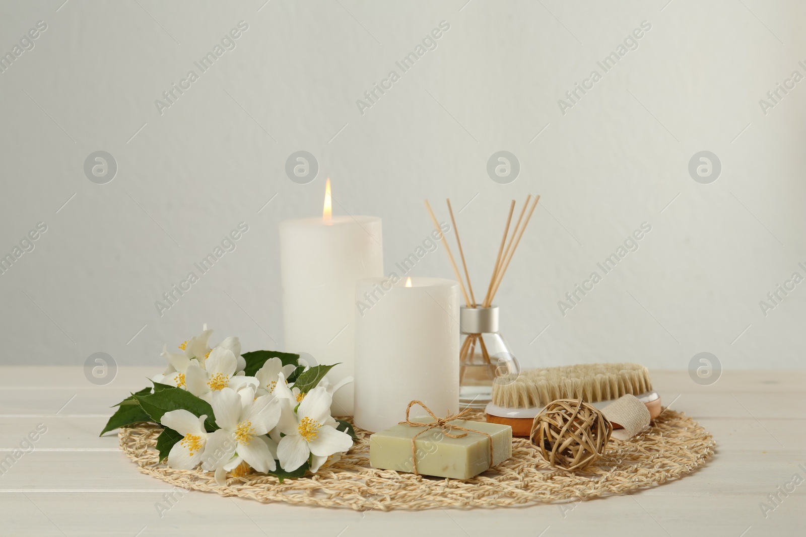 Photo of Composition with beautiful jasmine flowers, soap and burning candles on white wooden table