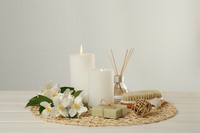 Composition with beautiful jasmine flowers, soap and burning candles on white wooden table