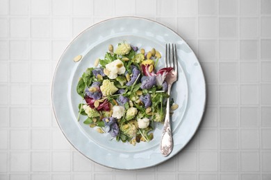 Delicious salad with cauliflower and pumpkin seeds served on white tiled table, top view