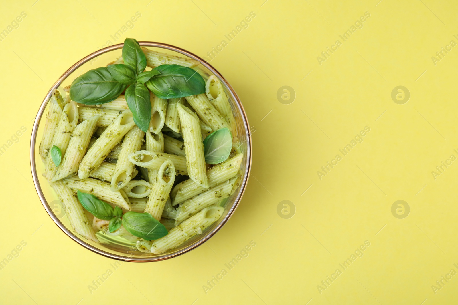 Photo of Delicious pasta with pesto sauce and basil on yellow background, top view. Space for text