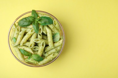 Delicious pasta with pesto sauce and basil on yellow background, top view. Space for text