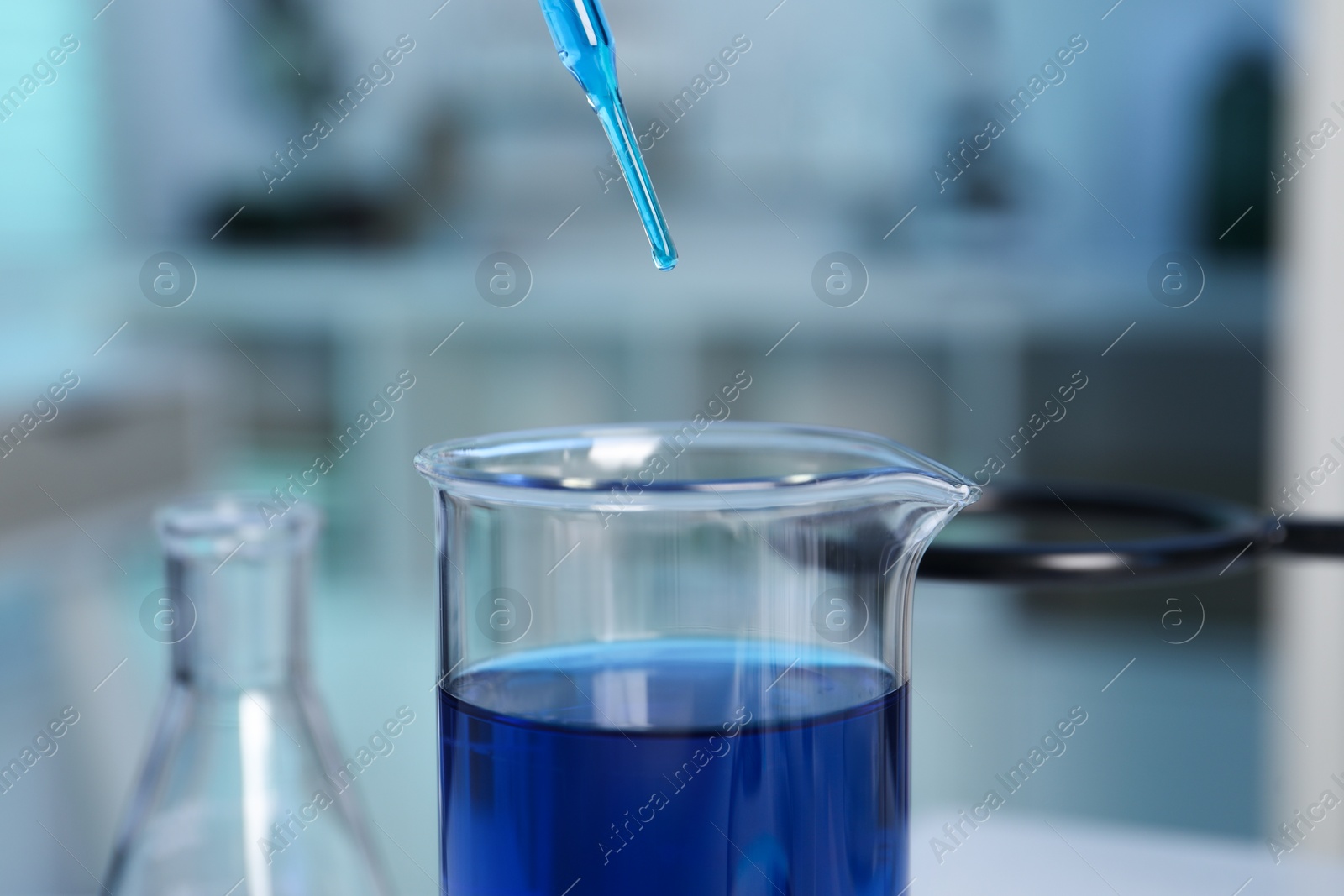 Photo of Laboratory analysis. Dripping blue liquid into beaker on table, closeup