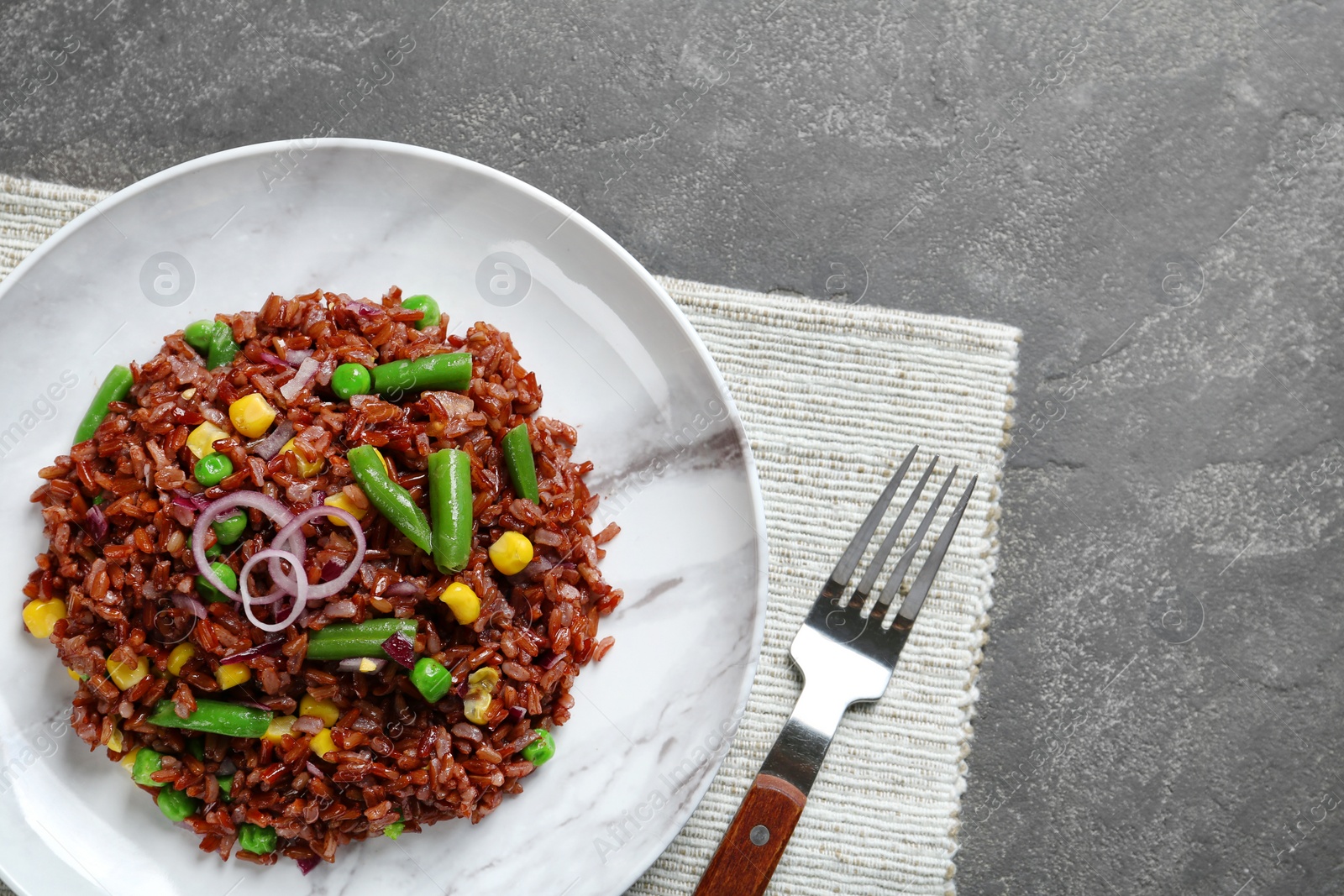 Photo of Plate of boiled brown rice with vegetables served on table, top view. Space for text