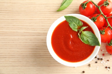 Photo of Bowl of tasty tomato sauce with basil on wooden table, flat lay. Space for text