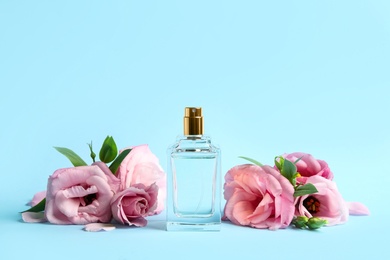 Photo of Bottle of perfume and beautiful flowers on light blue background