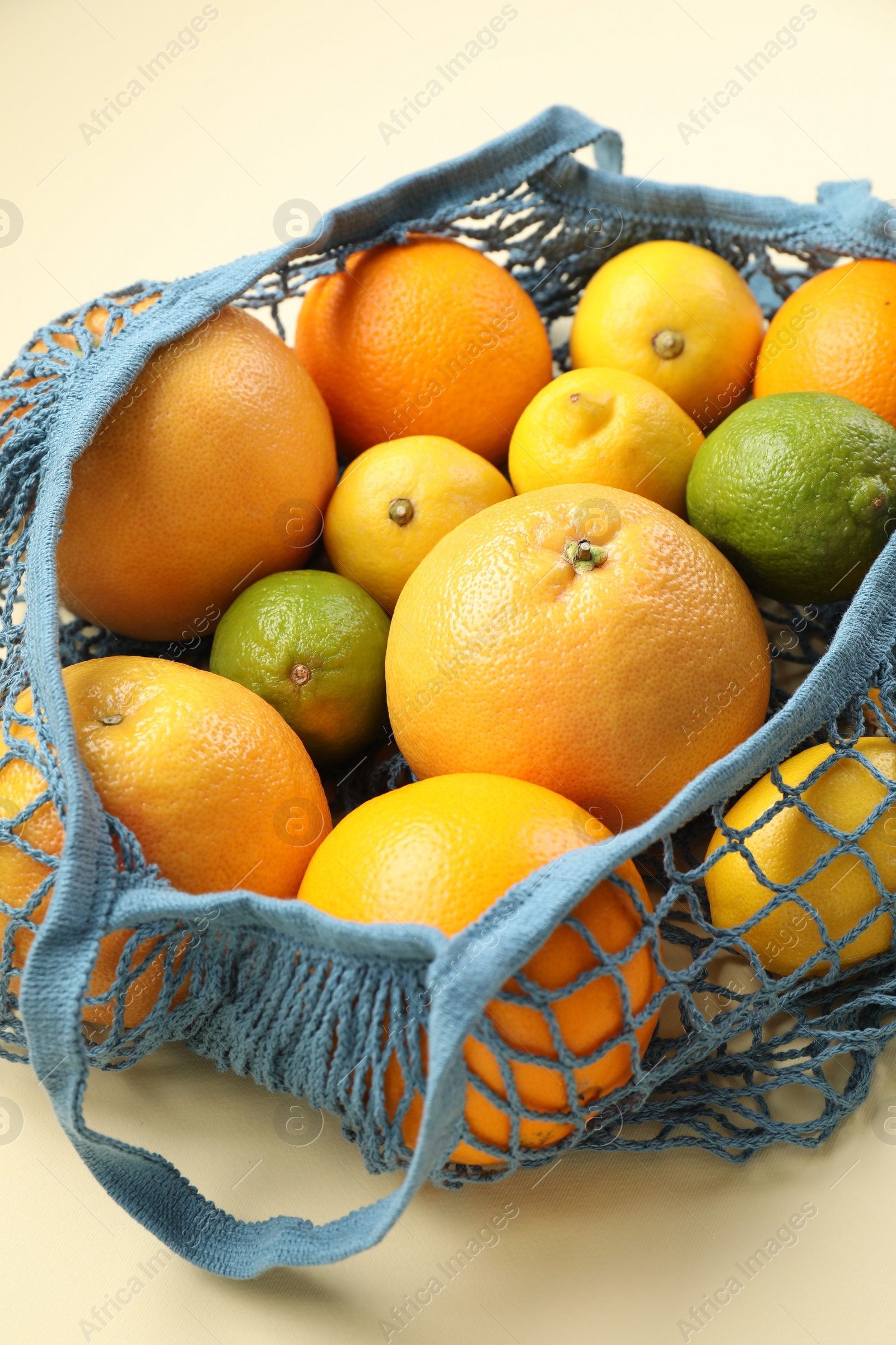 Photo of String bag with different fruits on beige background, closeup