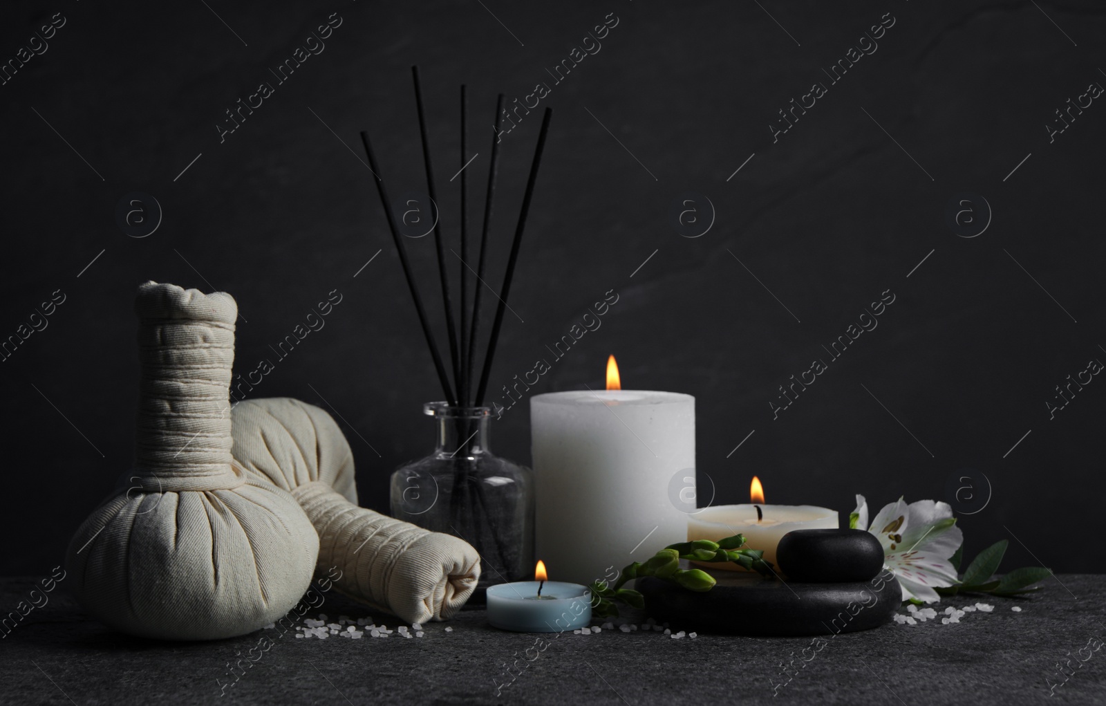 Photo of Beautiful spa composition with different care products and burning candles on dark grey table against black background. Space for text