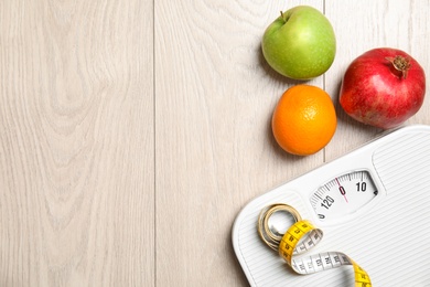 Photo of Flat lay composition with scales, measuring tape, fruits and space for text on wooden background. Weight loss
