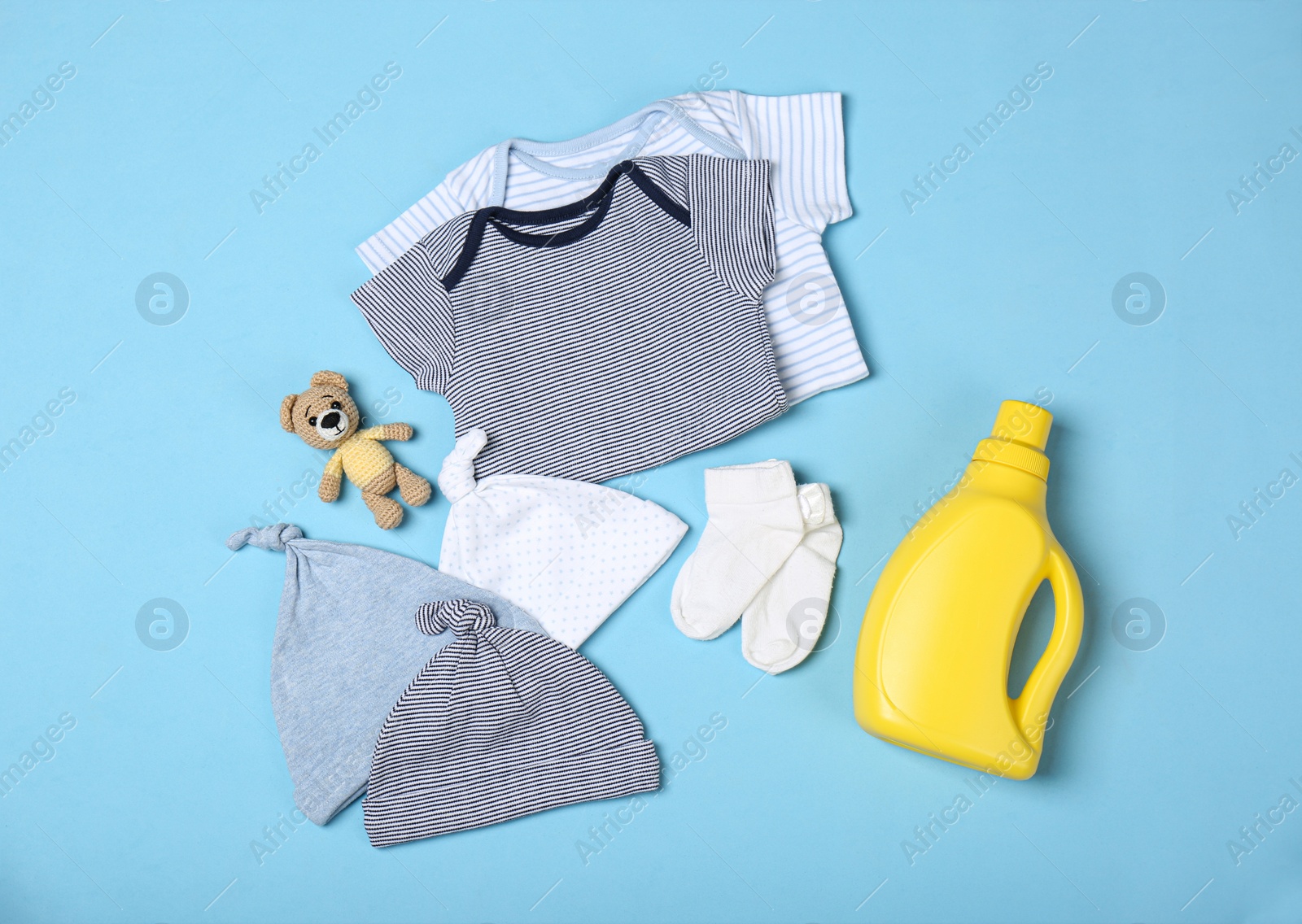 Photo of Flat lay composition with bottle of detergent and children's clothes on light blue background