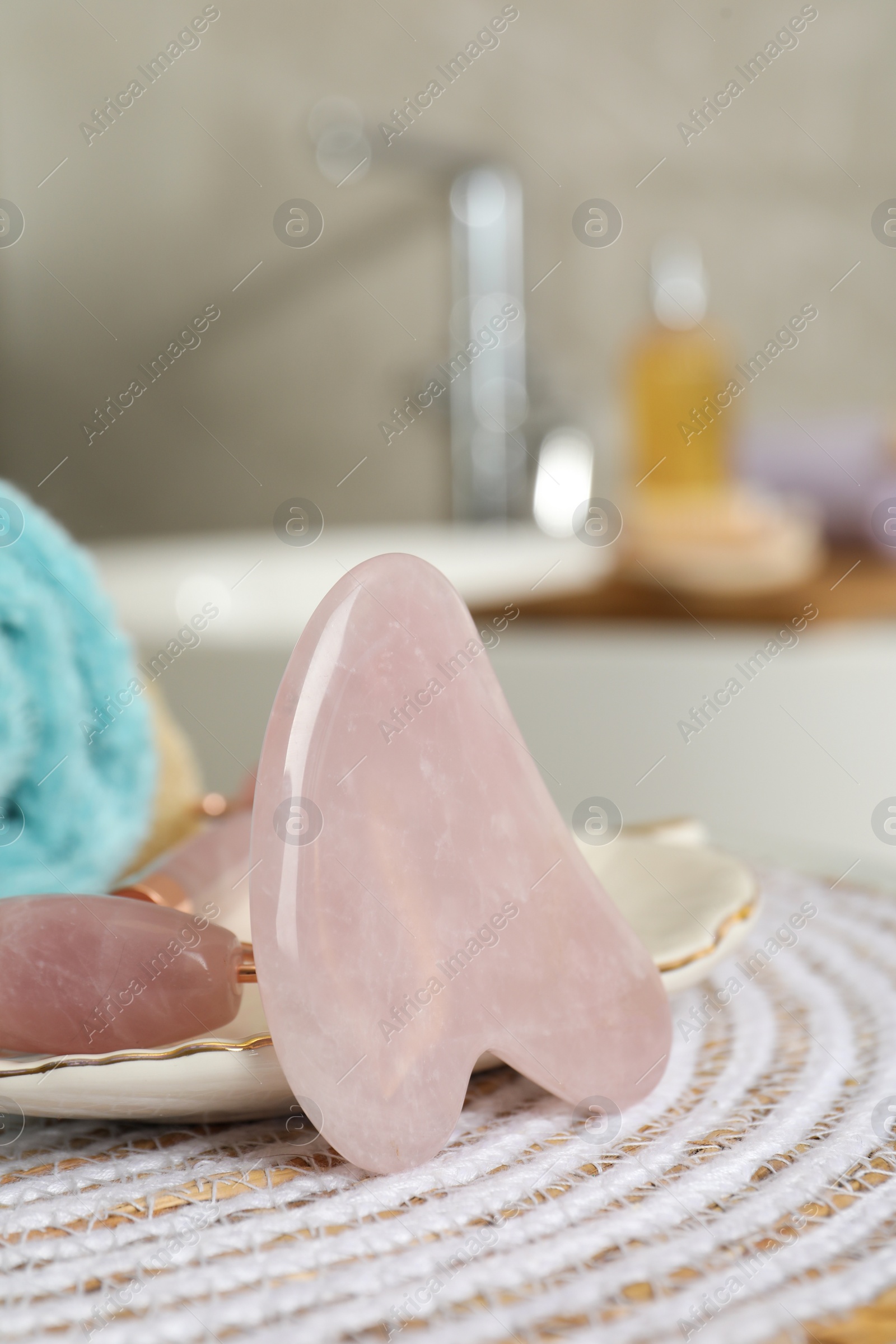 Photo of Rose quartz gua sha tool and natural face roller on table in bathroom, closeup