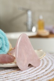 Rose quartz gua sha tool and natural face roller on table in bathroom, closeup