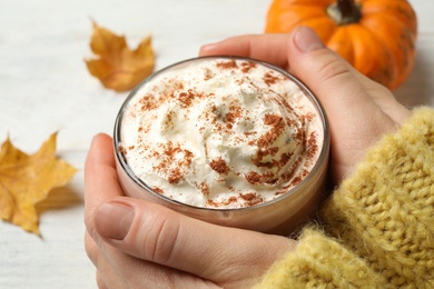 Photo of Woman holding tasty pumpkin latte at white table, closeup