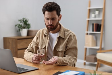 Man with pill and glass of water suffering from headache at workplace