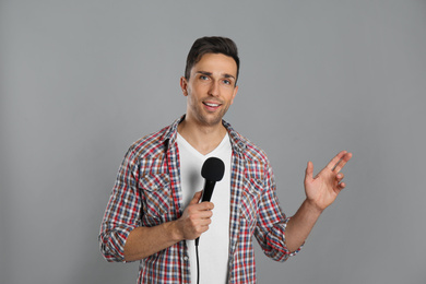 Young male journalist with microphone on grey background