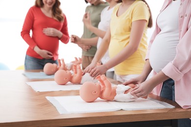 Pregnant women learning how to swaddle baby at courses for expectant mothers indoors, closeup