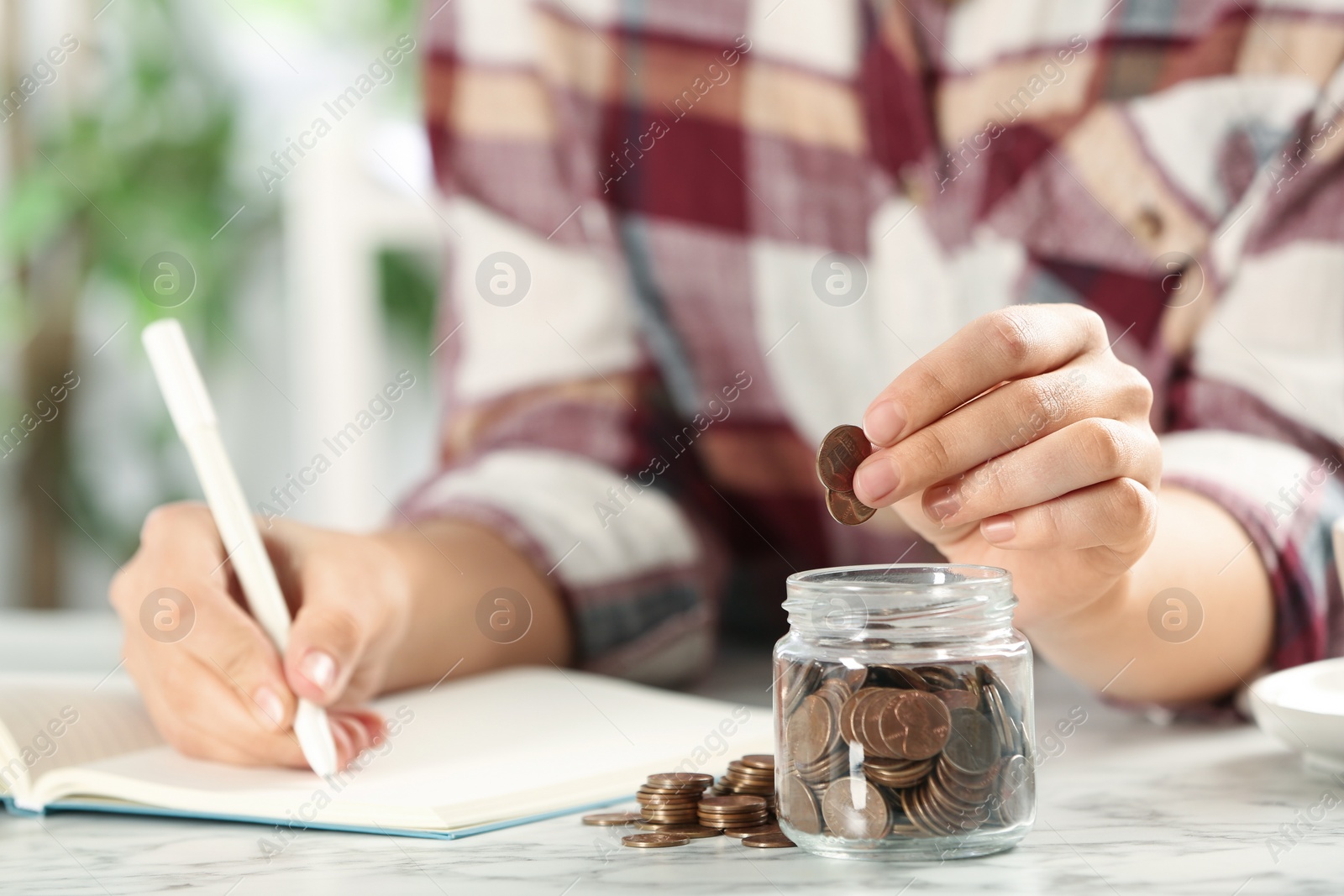 Photo of Woman putting money into glass jar at white marble table, closeup