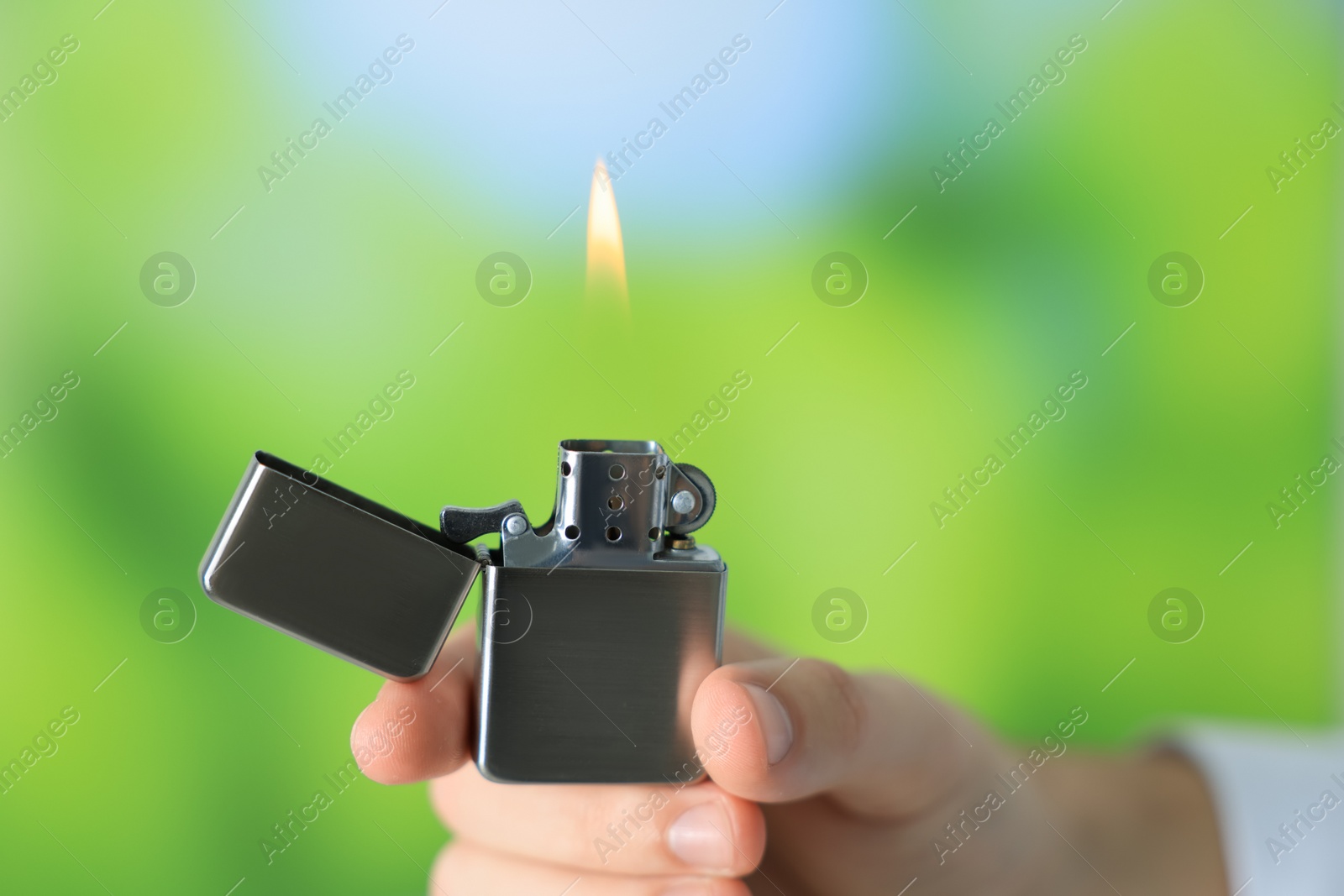 Photo of Man holding lighter with burning flame against blurred green background, closeup