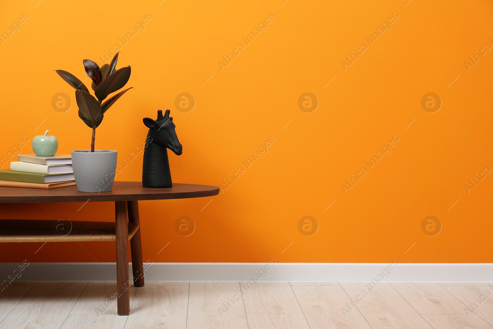 Photo of Wooden coffee table with different decor near orange wall indoors, space for text. Stylish interior design