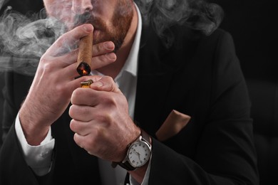 Photo of Man lightning cigar on black background, closeup