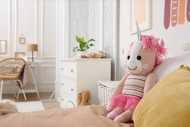 Photo of Toy unicorn and pillows on bed in child room. Interior design