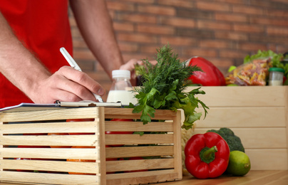 Photo of Man with fresh products at table indoors, closeup. Food delivery service