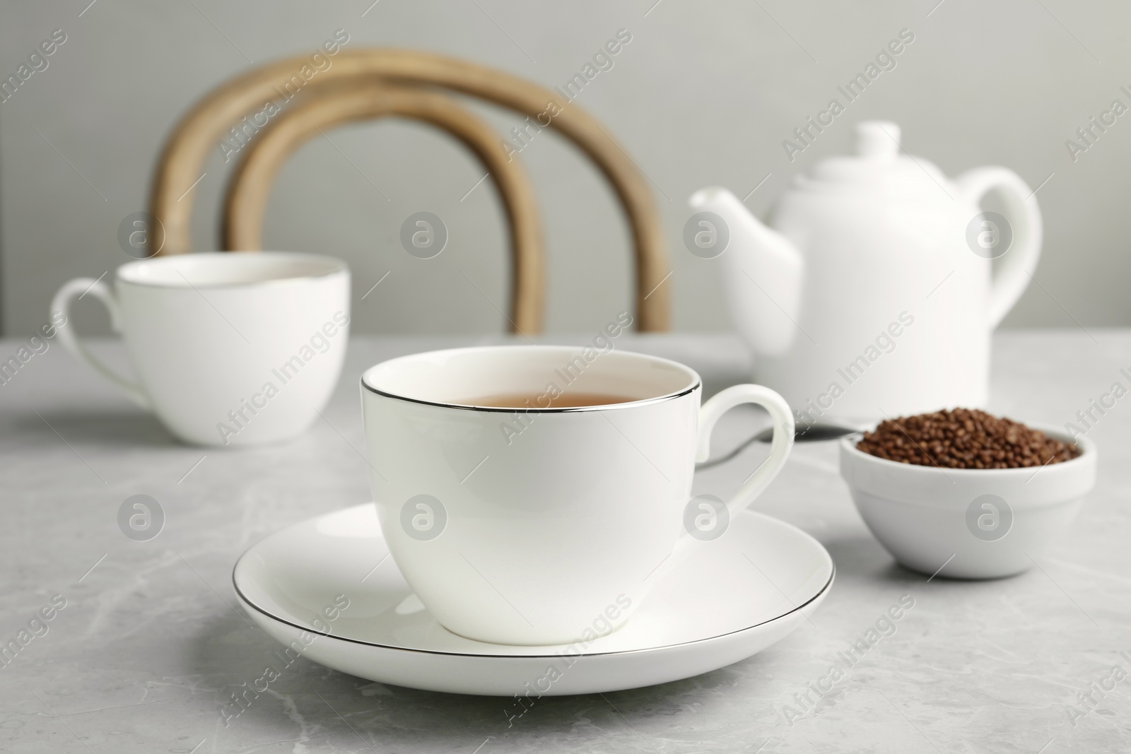 Photo of Cup of buckwheat tea and granules on light grey marble table