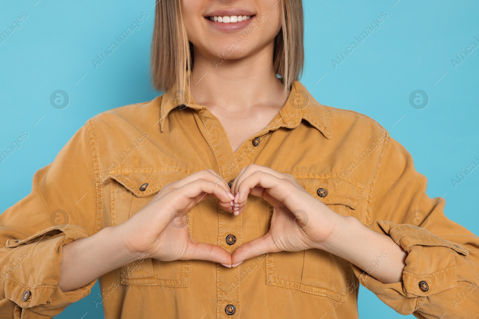 Photo of Young woman making heart with hands on turquoise background, closeup. Volunteer concept