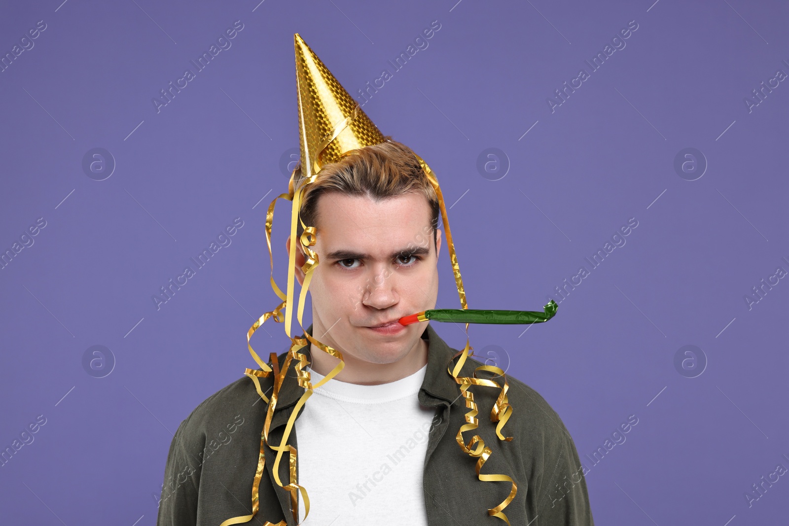 Photo of Sad young man with party hat and blower on purple background
