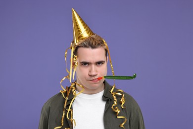 Photo of Sad young man with party hat and blower on purple background