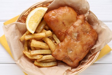 Photo of Tasty fish, chips and lemon on white wooden table, top view