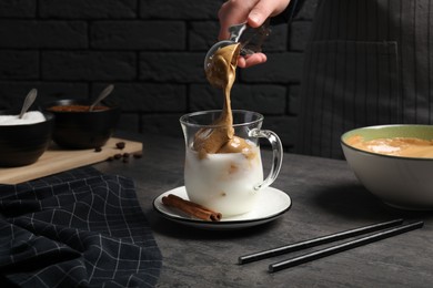 Woman making dalgona coffee at grey table, closeup