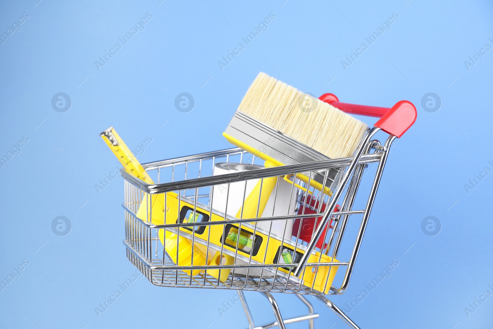 Photo of Small shopping cart with paint and renovation equipment on light blue background