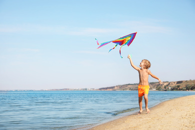 Photo of Cute little child with kite running at beach on sunny day