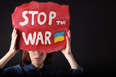 Photo of Sad woman holding poster with words Stop the War on black background. Space for text
