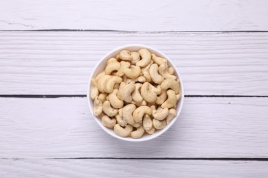 Photo of Tasty cashew nuts in bowl on white wooden table, top view