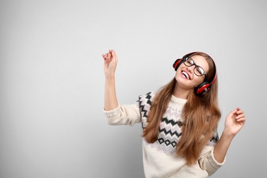 Young woman listening to music with headphones on grey background, space for text