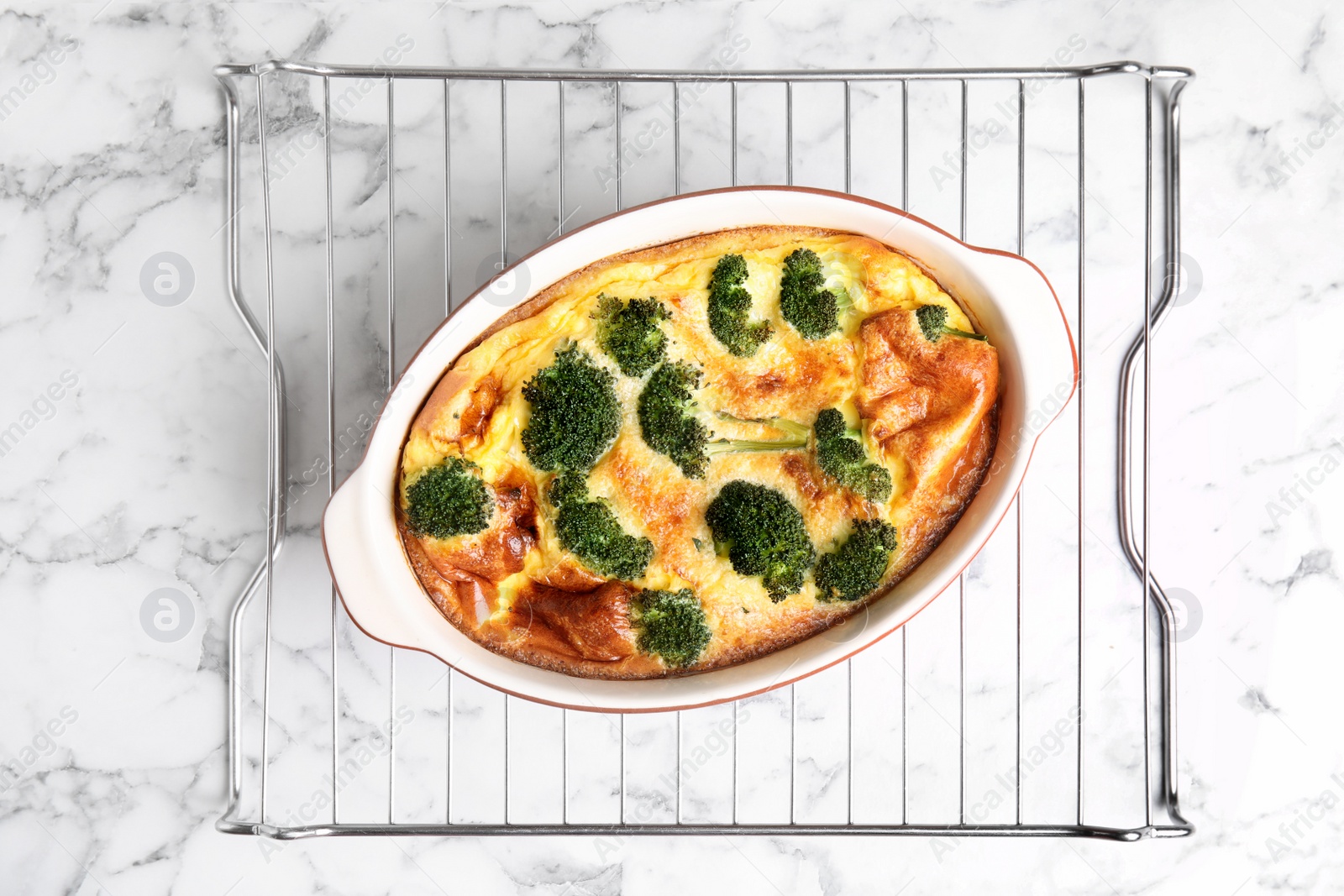 Photo of Tasty broccoli casserole in baking dish on cooling rack, top view