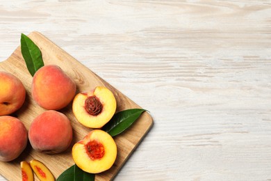 Photo of Cut and whole fresh ripe peaches with green leaves on light wooden table, top view. Space for text