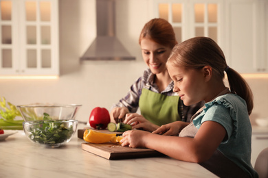 Photo of Mother and daughter cooking salad together in kitchen