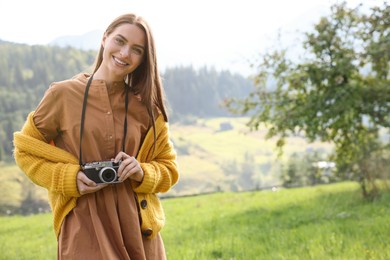 Happy woman with camera on meadow in mountains