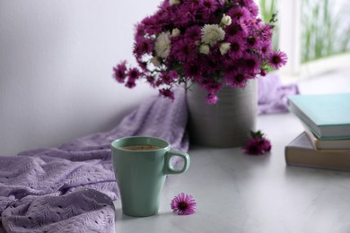 Photo of Cup of aromatic coffee, beautiful flowers and violet cloth on white table