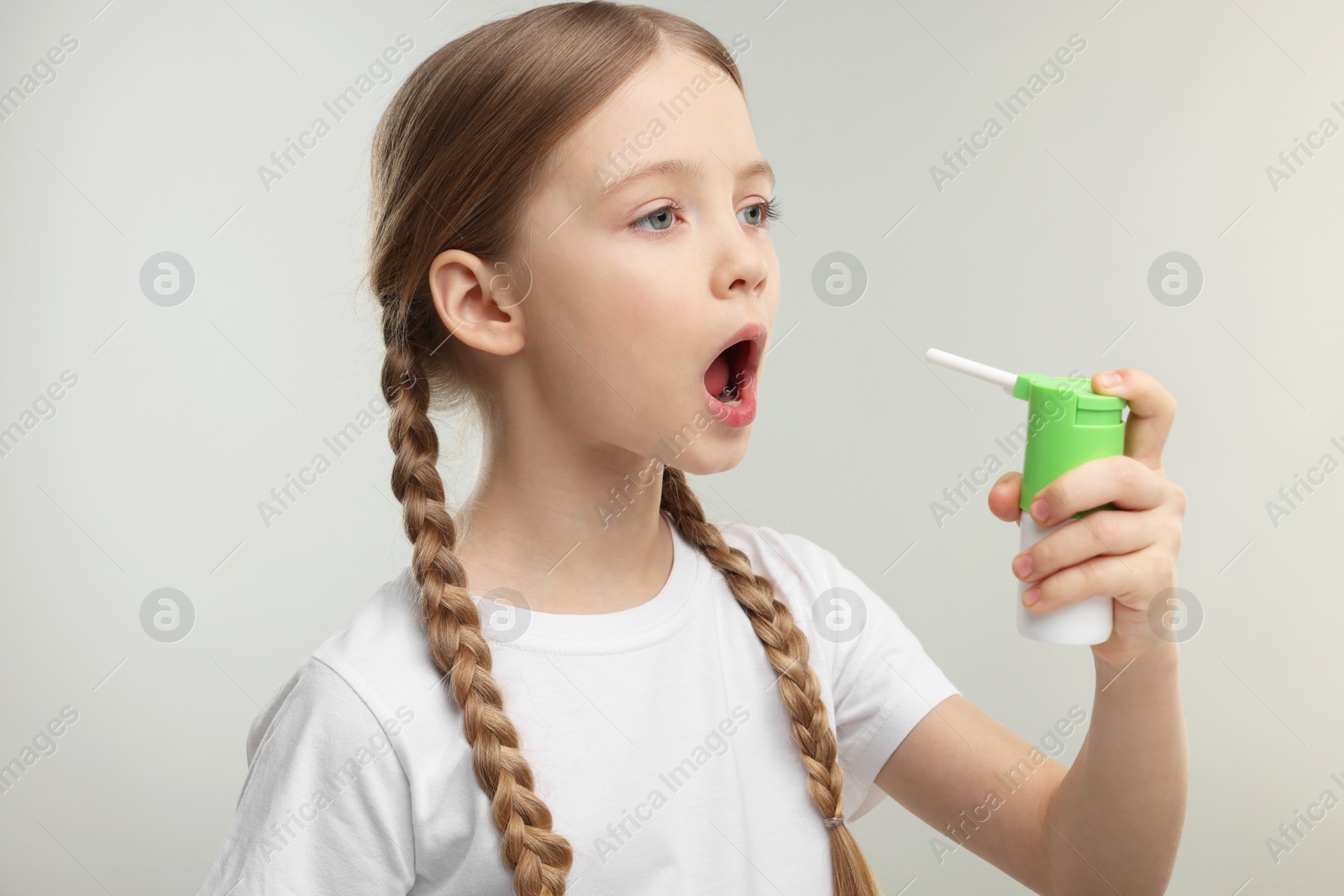 Photo of Little girl using throat spray on light grey background