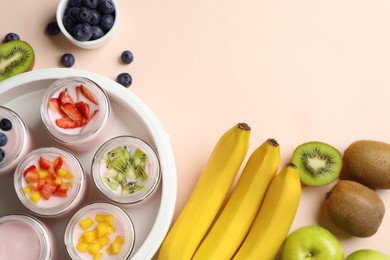 Photo of Yogurt maker with jars and different fruits on light pink background, flat lay